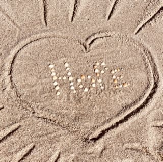 A heart drawn in the sand with " hate " written on it.